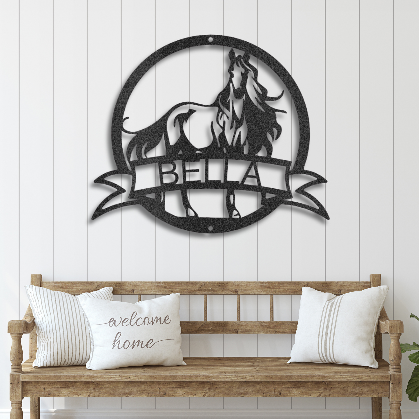 Decorative metal wall art with horse design and customized name 'Bella' above a wooden bench with pillows.