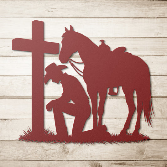 metal wall art of a cowboy kneeling in prayer by a cross with his saddled horse, displayed on a rustic white wood background.